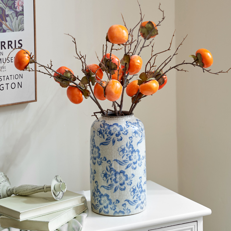 Large blue and white floral porcelain vase holding orange persimmon branches on a white cabinet.