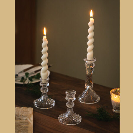 Swirled glass candle holders on wooden dining table with lit taper candles